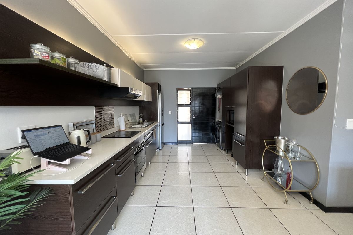 Modern galley-style kitchen featuring dark wood cabinetry, stone countertops, integrated appliances, and tiled flooring, offering a clean and functional workspace.