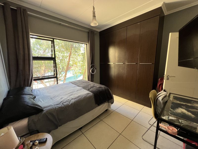 A well-lit bedroom featuring large windows, tiled flooring, and a spacious built-in wardrobe providing ample storage.