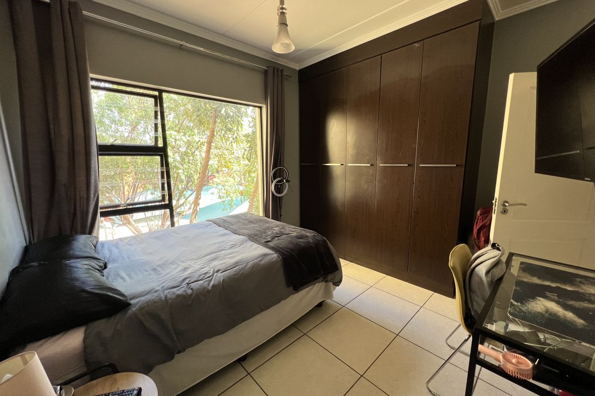A well-lit bedroom featuring large windows, tiled flooring, and a spacious built-in wardrobe providing ample storage.