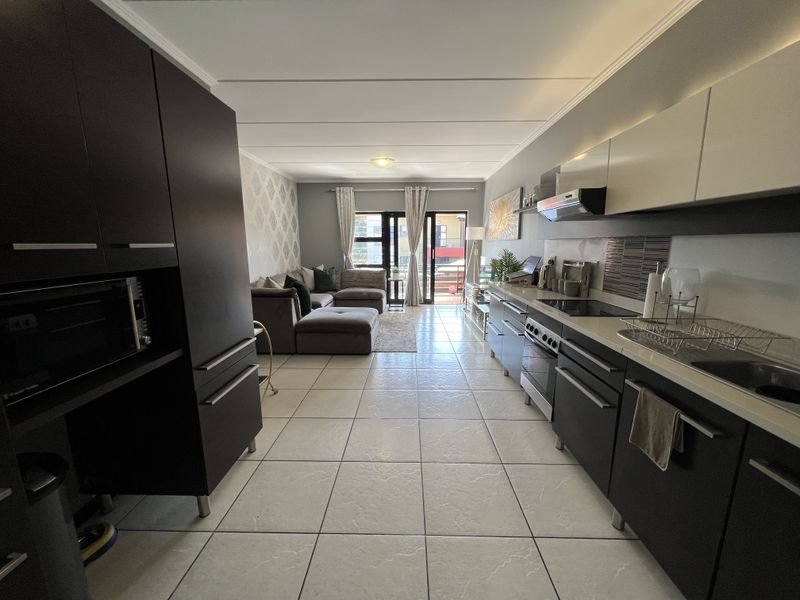 Modern open-plan kitchen and living area featuring dark cabinetry, integrated appliances, tiled flooring, and direct access to a balcony through sliding glass doors.