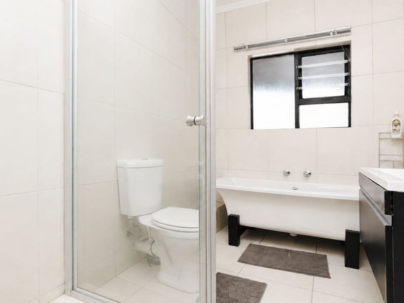 A clean, modern bathroom featuring a freestanding bathtub, a separate glass-enclosed shower, a vanity with basin, and neutral wall and floor tiling.