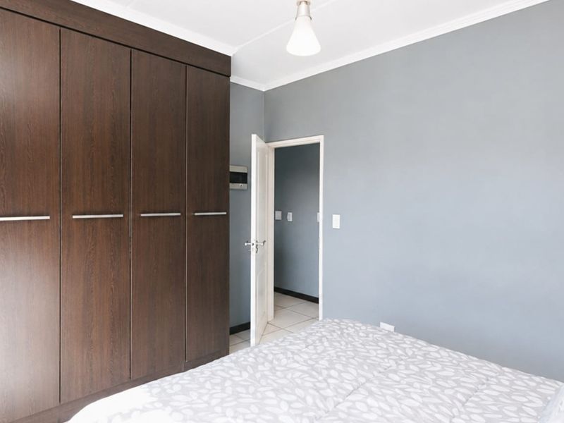 A well-maintained bedroom featuring dark wood built-in wardrobes, neutral grey walls, and a clean, functional layout.