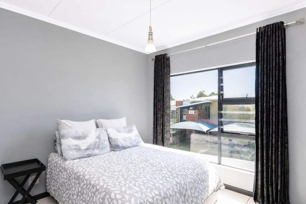 A well-lit bedroom featuring neutral grey walls, a large window with natural light, and modern pendant lighting.