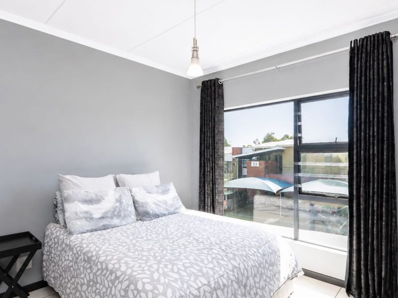A well-lit bedroom featuring neutral grey walls, a large window with natural light, and modern pendant lighting.