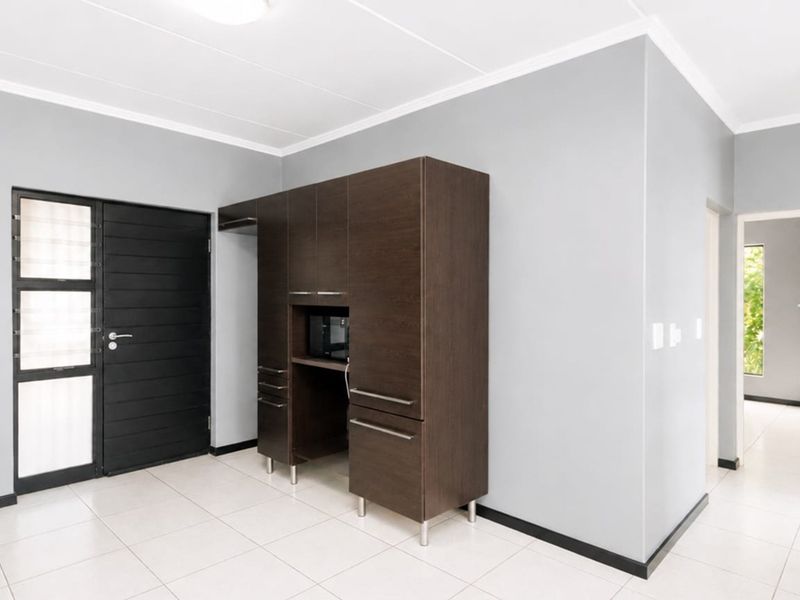 A clean and modern entrance area featuring neutral grey walls, tiled flooring, and a dark wood built-in storage unit.