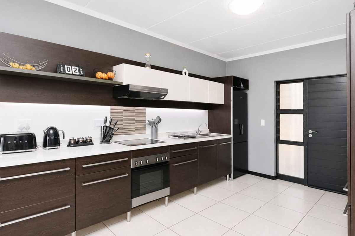 Modern kitchen featuring dark wood cabinetry, white countertops, integrated appliances, and tiled flooring with direct access to an exterior door.