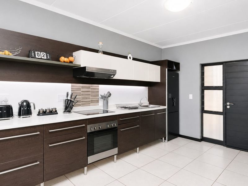 Modern kitchen featuring dark wood cabinetry, white countertops, integrated appliances, and tiled flooring with direct access to an exterior door.