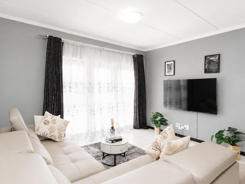 A well-maintained living room featuring neutral grey walls, tiled flooring, and a large sliding glass door that provides ample natural light.