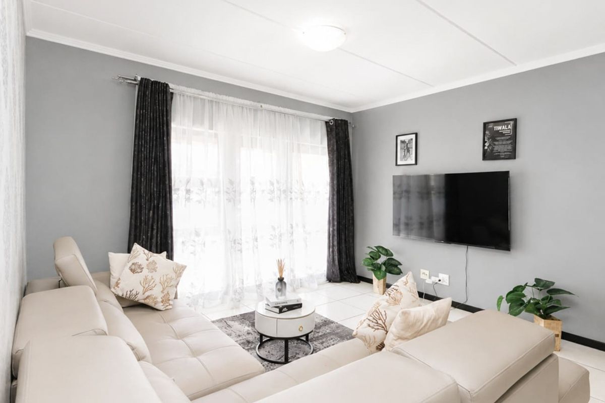 A well-maintained living room featuring neutral grey walls, tiled flooring, and a large sliding glass door that provides ample natural light.
