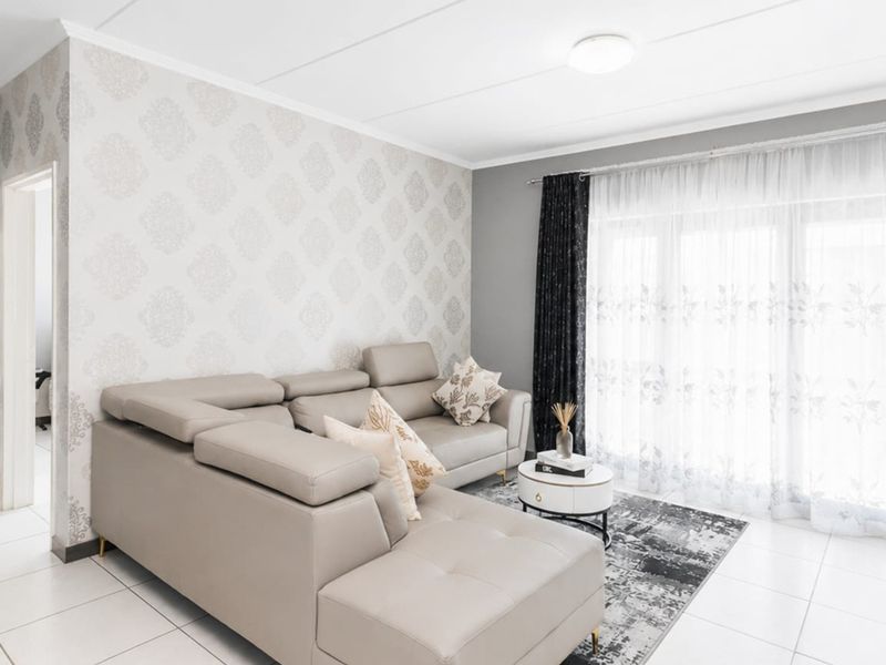 A bright living room featuring neutral tiled flooring, patterned wallpaper, and a large sliding glass door providing natural light.