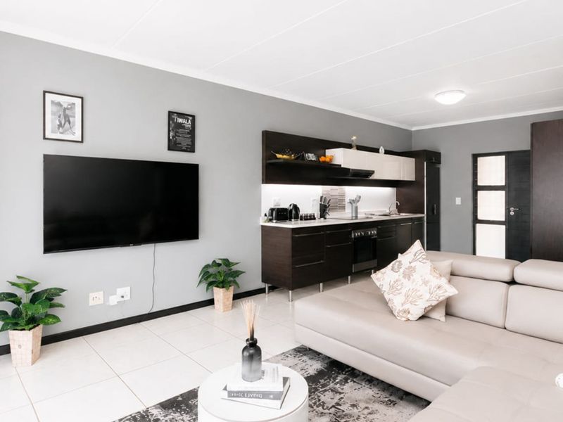 Modern open-plan living area featuring a sleek kitchen with dark cabinetry, integrated appliances, and light tiled flooring throughout the space.