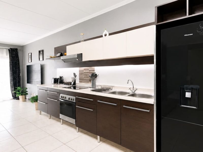 Modern open-plan kitchen featuring dark wood and cream cabinetry, integrated appliances, tiled flooring, and sleek under-cabinet lighting, flowing into the living area.
