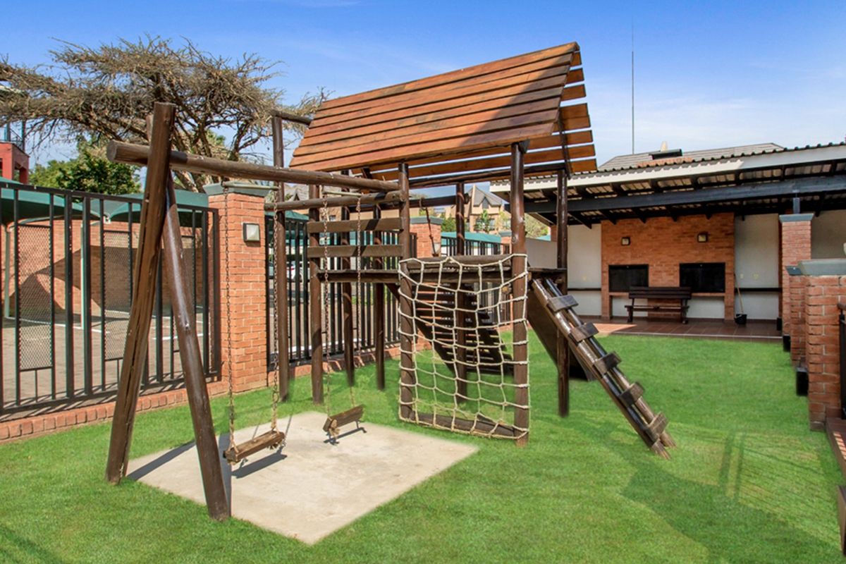 Communal outdoor area featuring a well-maintained lawn, playground equipment, and a covered patio with a built-in braai facility.