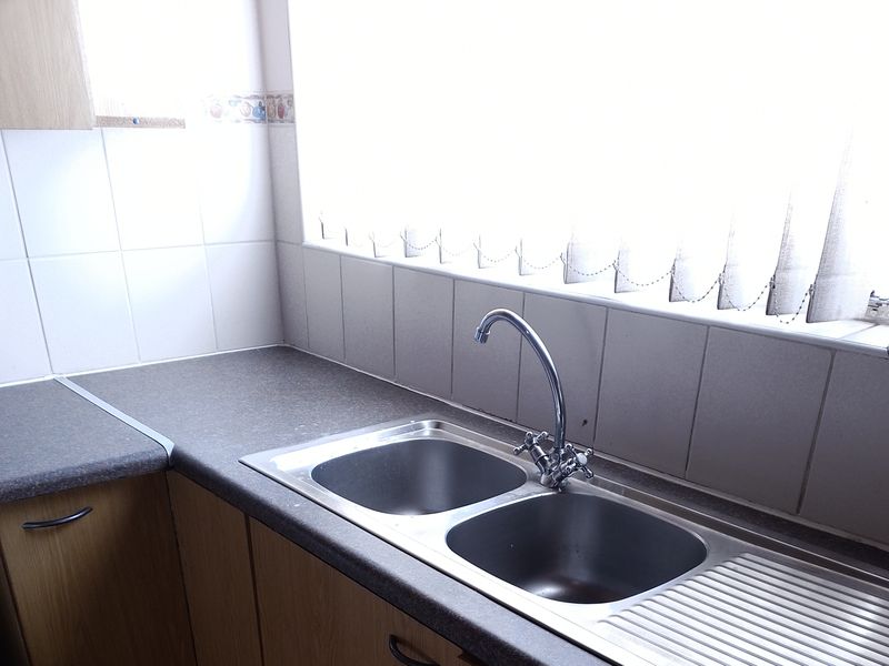 A functional kitchen area featuring a double bowl stainless steel sink, chrome mixer tap, laminate countertops, and tiled splashback.