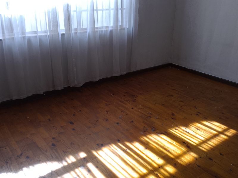An empty bedroom featuring original timber flooring and a window with security bars, receiving natural light.