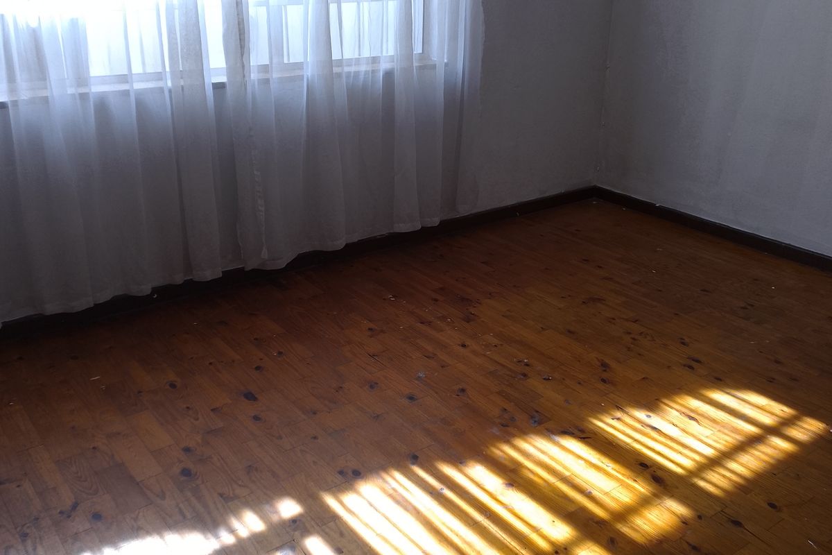 An empty bedroom featuring original timber flooring and a window with security bars, receiving natural light.