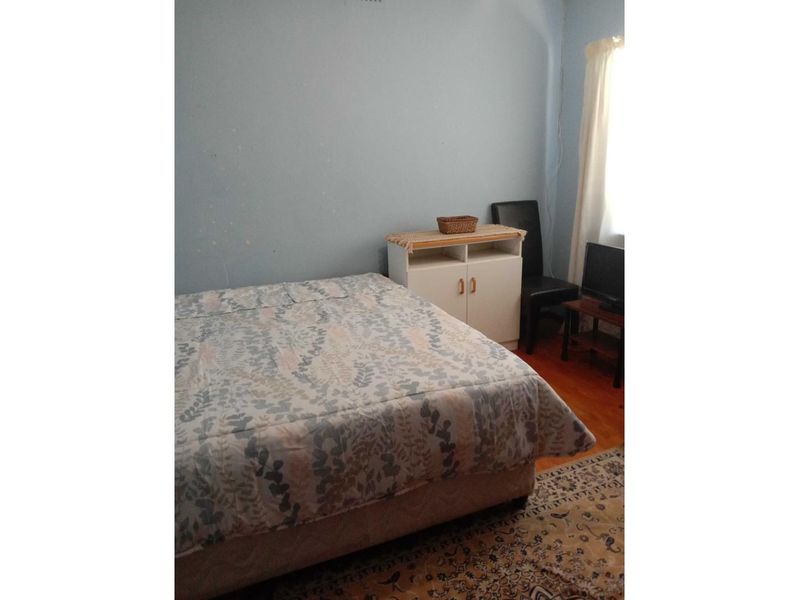 A bedroom featuring hardwood flooring and a window, currently showing signs of wear on the walls requiring cosmetic attention.