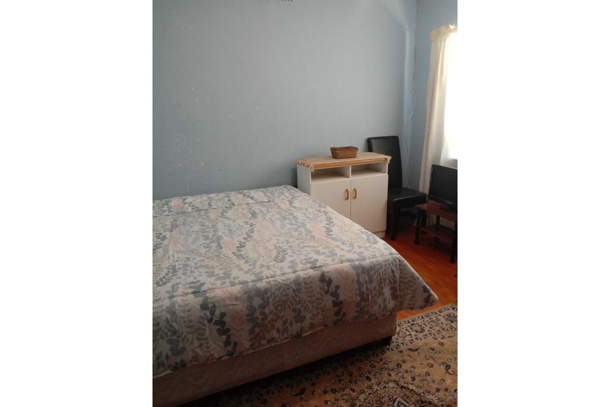 A bedroom featuring hardwood flooring and a window, currently showing signs of wear on the walls requiring cosmetic attention.