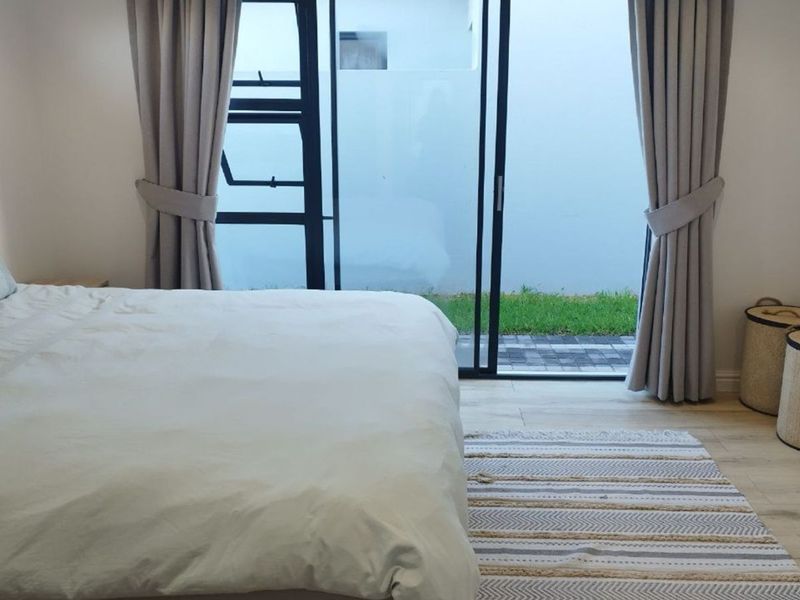 A well-maintained bedroom featuring light laminate flooring and a large sliding glass door providing direct access to a private outdoor garden area.