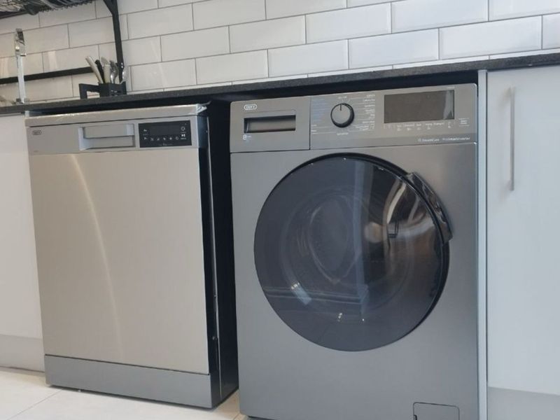 A modern laundry area featuring a subway tile backsplash, granite countertops, and integrated appliances including a dishwasher and front-load washing machine.