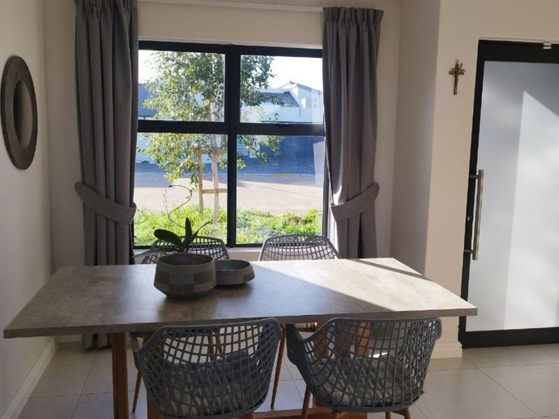 A bright dining area featuring tiled flooring, a large window with natural light, and a modern frosted glass door.