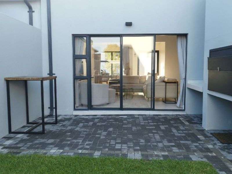A paved outdoor patio area featuring a built-in braai and sliding glass doors providing seamless access to the interior living space.