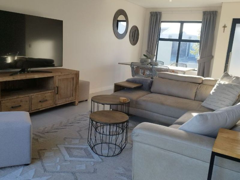 A well-maintained living room featuring neutral tones, recessed downlighting, and large aluminium-framed windows that provide ample natural light.