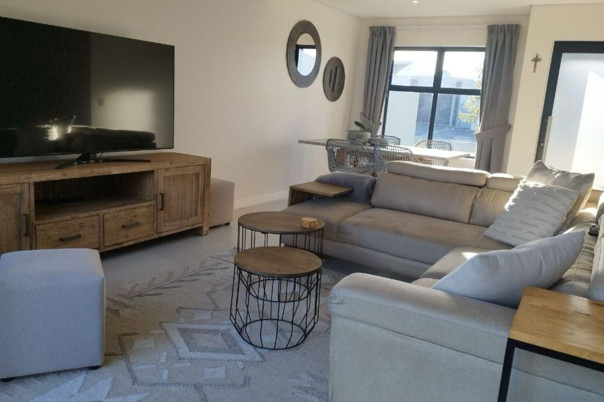 A well-maintained living room featuring neutral tones, recessed downlighting, and large aluminium-framed windows that provide ample natural light.