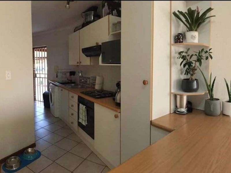 A functional kitchen featuring built-in cabinetry, gas hob, oven, and tiled flooring, with an adjacent laundry area and security gate access.