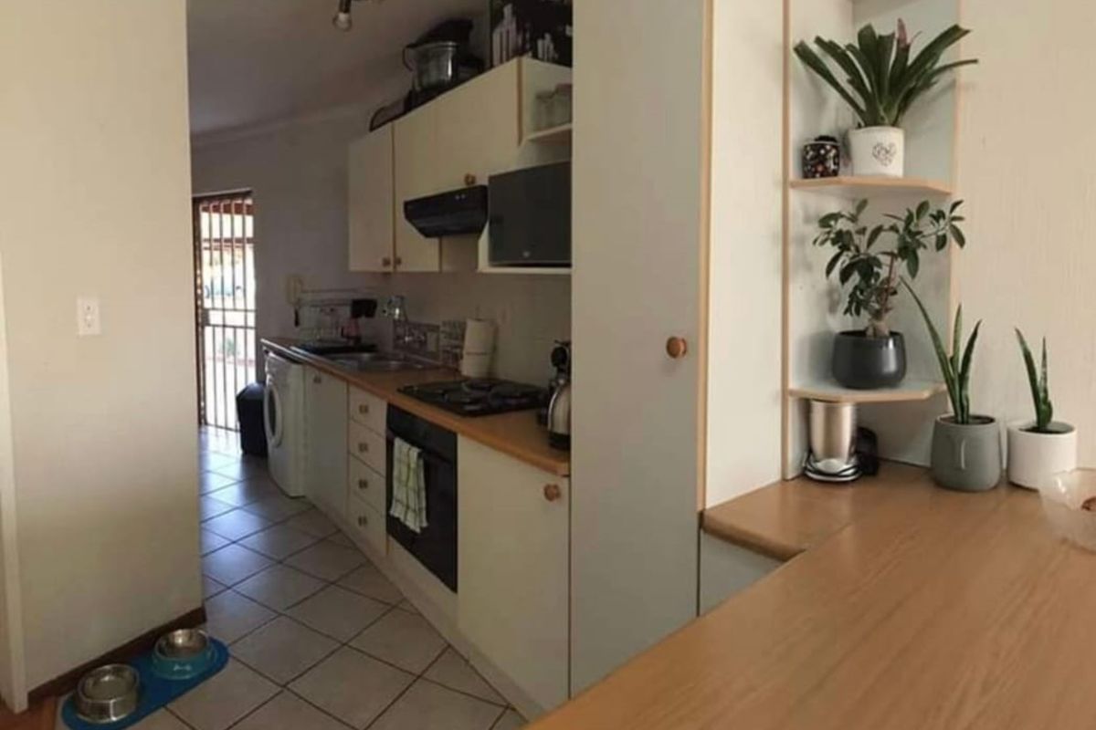 A functional kitchen featuring built-in cabinetry, gas hob, oven, and tiled flooring, with an adjacent laundry area and security gate access.