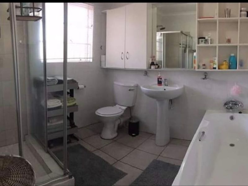 A functional bathroom featuring a separate shower enclosure, bathtub, pedestal basin, and built-in wall storage cabinetry with tiled flooring.