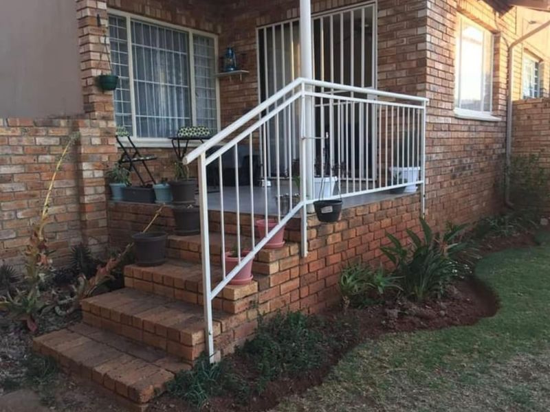 A raised brick patio area featuring a metal safety railing, brick stairs, and secure access points to the townhouse interior.