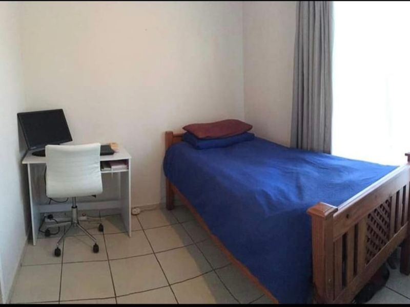 A compact bedroom featuring tiled flooring and neutral walls, suitable for a single bed and study area.