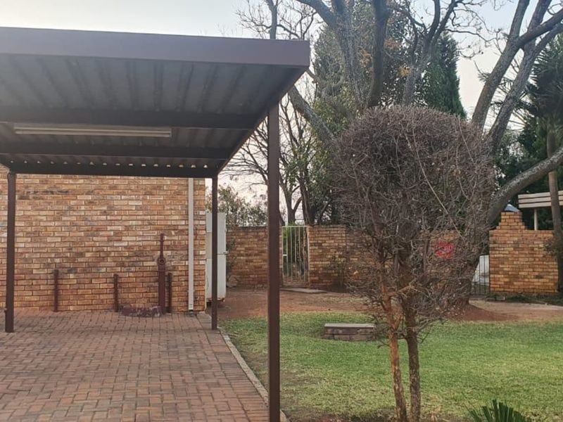 Front exterior view of the townhouse featuring a covered carport, brick paved driveway, and established garden area with security features.