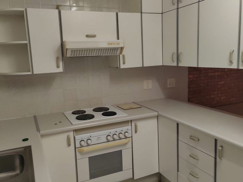 A functional kitchen featuring white built-in cabinetry, an integrated electric hob and oven, extractor fan, and a stainless steel sink with tiled backsplash.