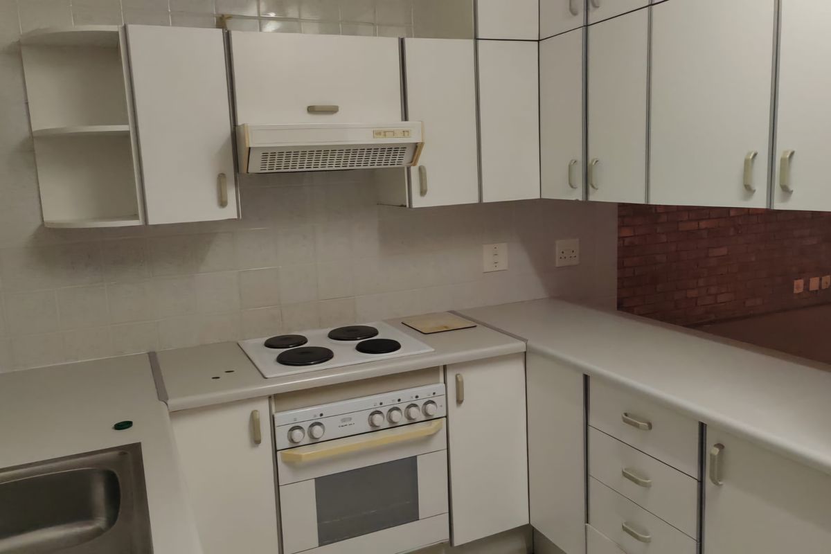 A functional kitchen featuring white built-in cabinetry, an integrated electric hob and oven, extractor fan, and a stainless steel sink with tiled backsplash.