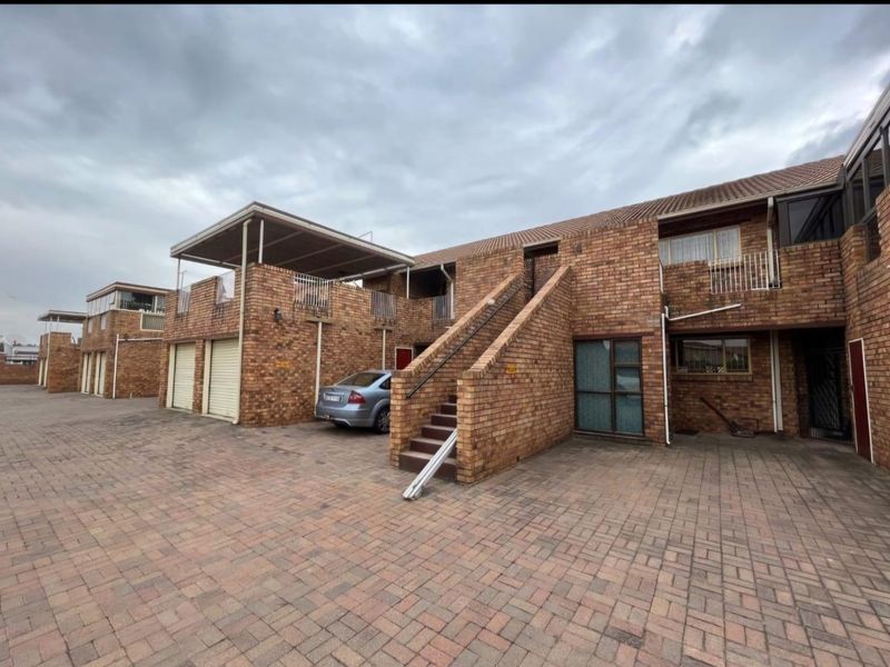 Exterior view of a face brick apartment complex featuring a paved driveway, external staircase, and integrated garage units.