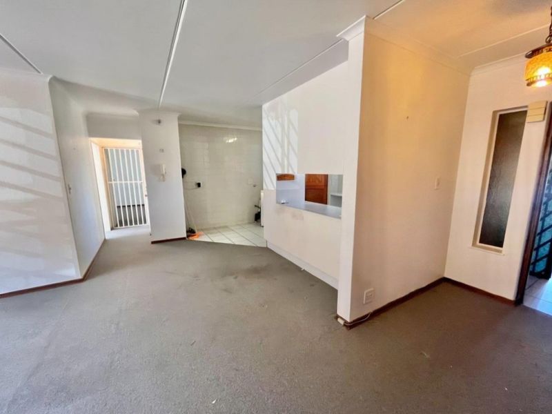 Open-plan living area featuring carpeted flooring, a pass-through kitchen window, and a secure entrance, offering a blank canvas for renovation.