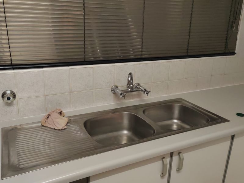 A functional kitchen area featuring a stainless steel double sink, wall-mounted tap, tiled splashback, and neutral under-counter cabinetry with laminate countertops.