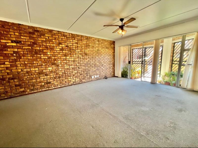 Spacious living area featuring an exposed brick wall, ceiling fan, and large sliding glass doors leading to an outdoor space.