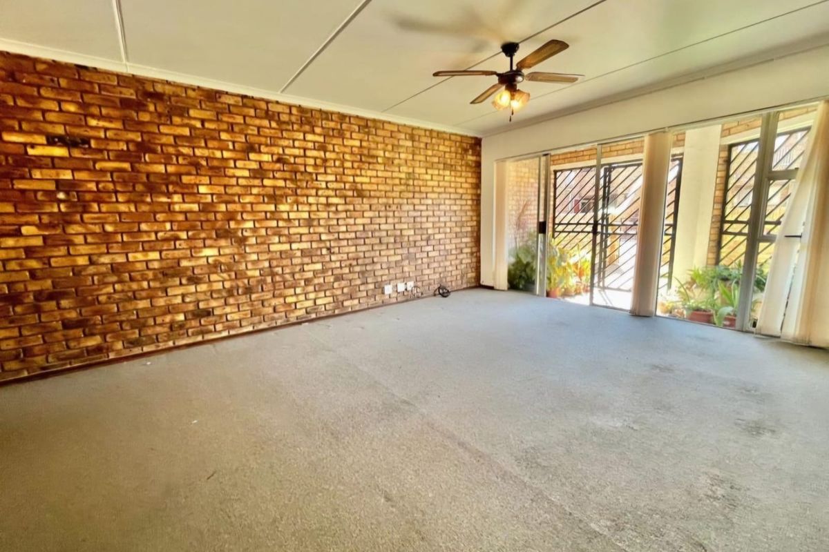 Spacious living area featuring an exposed brick wall, ceiling fan, and large sliding glass doors leading to an outdoor space.