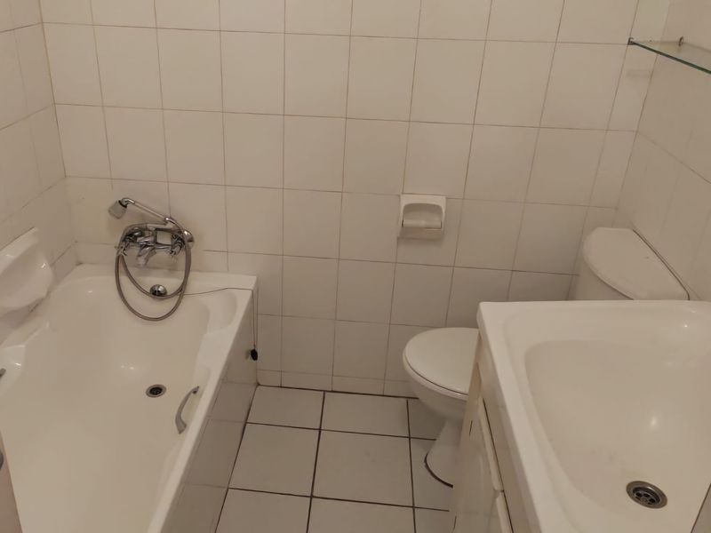 A compact bathroom featuring a standard bathtub with shower mixer, toilet, and vanity basin with white wall and floor tiling.