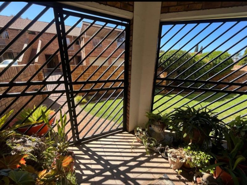 A covered patio area featuring tiled flooring, brick pillars, and secure metal security gates overlooking a private garden space.