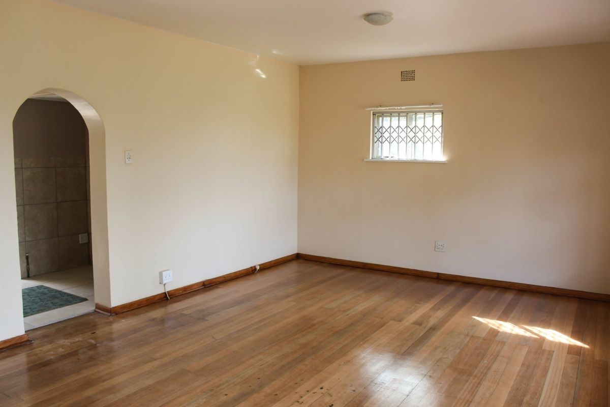 A vacant living room featuring polished timber flooring, an arched doorway leading to an adjacent space, and a window with security bars.