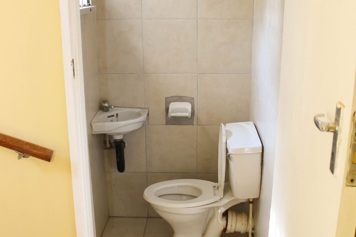 A compact guest bathroom featuring a standard toilet, wall-mounted corner basin, and neutral tiled finishes.