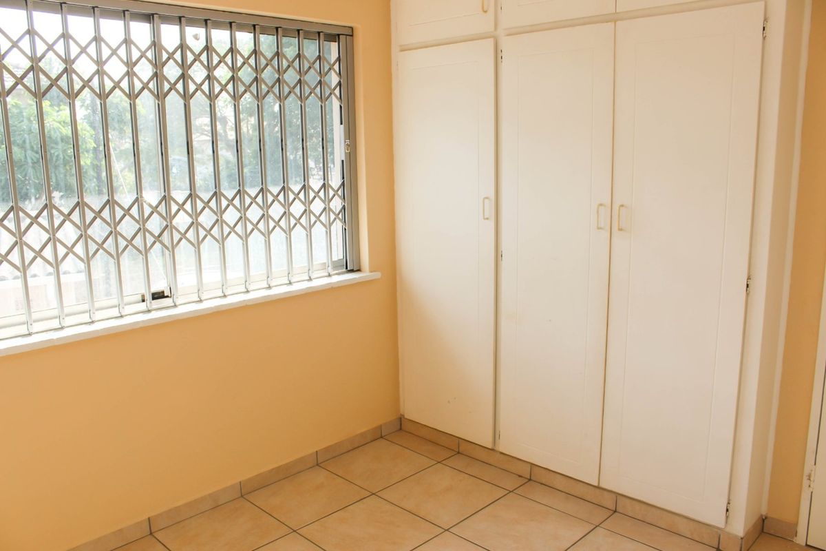 A bedroom featuring built-in cupboards and a window fitted with a metal security gate.
