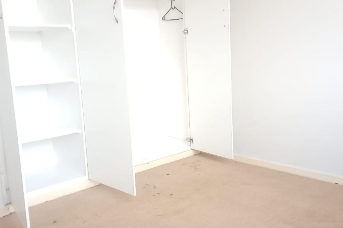 A bedroom featuring built-in white cabinetry with shelving and hanging space, finished with neutral carpeting.