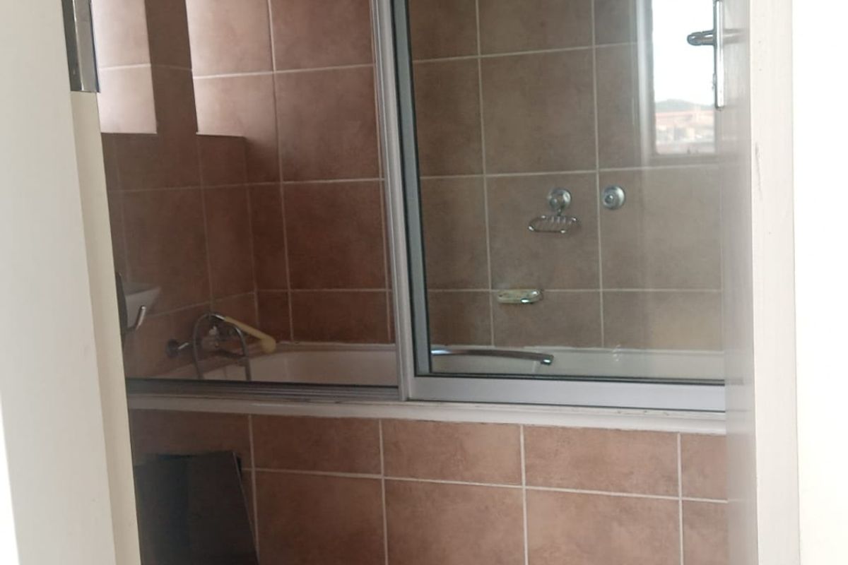 A functional bathroom featuring a combined bathtub and shower unit with sliding glass doors, tiled walls, and floor.