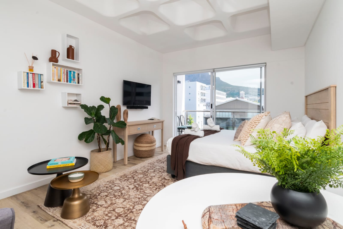 A bright, modern bedroom featuring a unique coffered ceiling, wood-look flooring, and a sliding glass door leading to a balcony with mountain views.