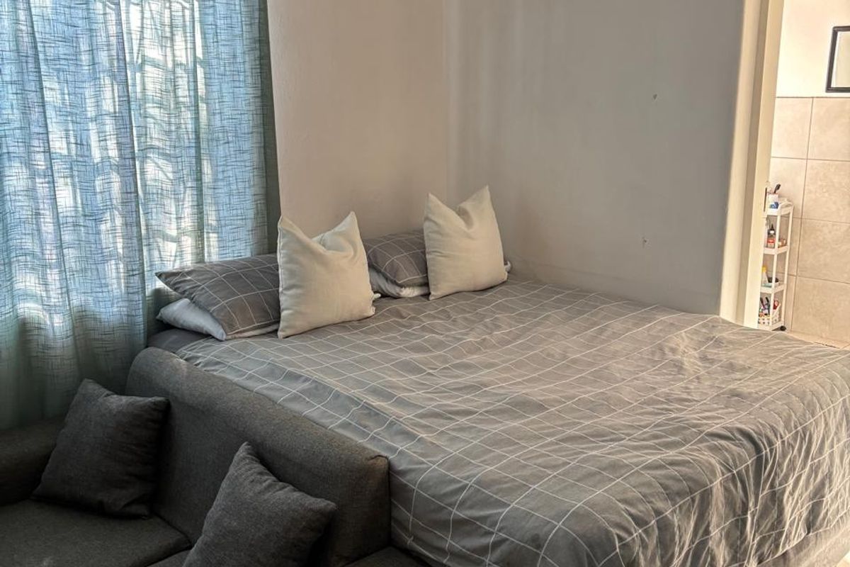 A bedroom featuring tiled flooring and a window with a curtain rod, showing signs of wear including wall cracks and exposed wiring.